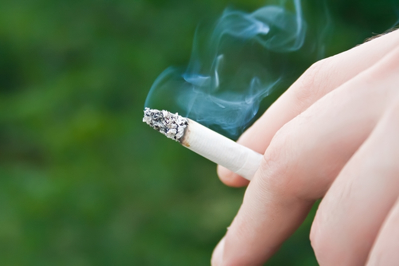 Lit cigarette emitting smoke between man's fingers.