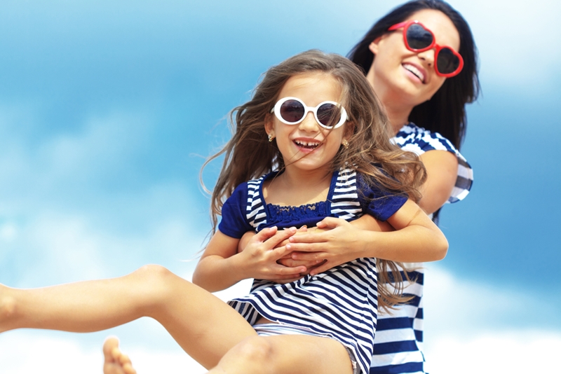 Mom swinging daughter around wearing sunglasses.
