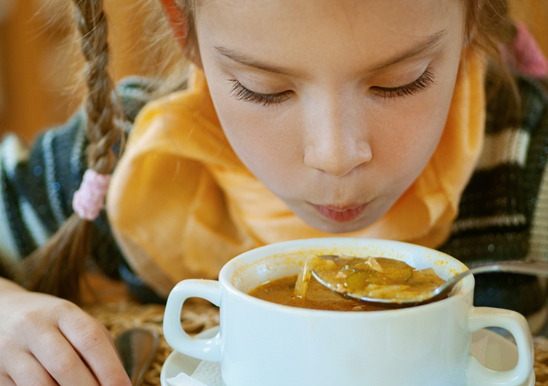Girl blowing on spoonful of hot soup.