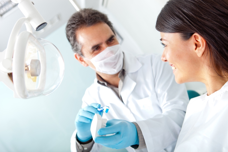 Dentist showing woman how to use toothbrush in office.