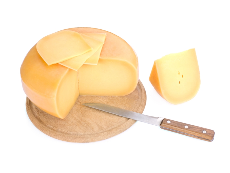 Block of cheese on cutting board sliced with knife.