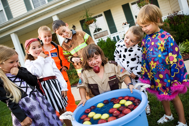 Little girl bobbing for apples at Halloween party.