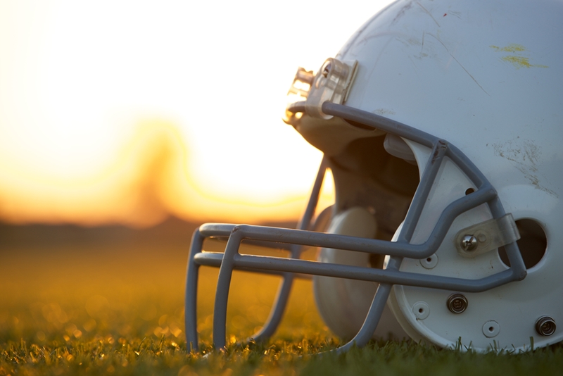 Football helmet sitting on grass with sunset background.