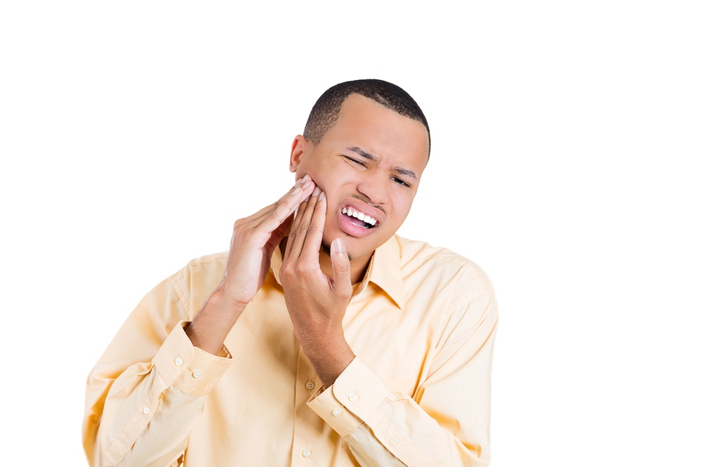 Young man in pain, indicating he has a toothache by holding the left side of his face