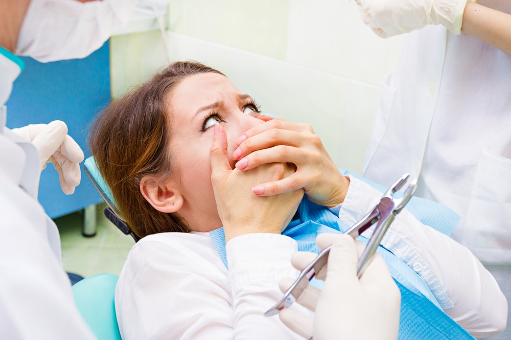 Overcoming Fear of the Dentist - Young terrified woman scared at dentist visit, sitting in chair, covering her mouth, doesn't want dental procedure