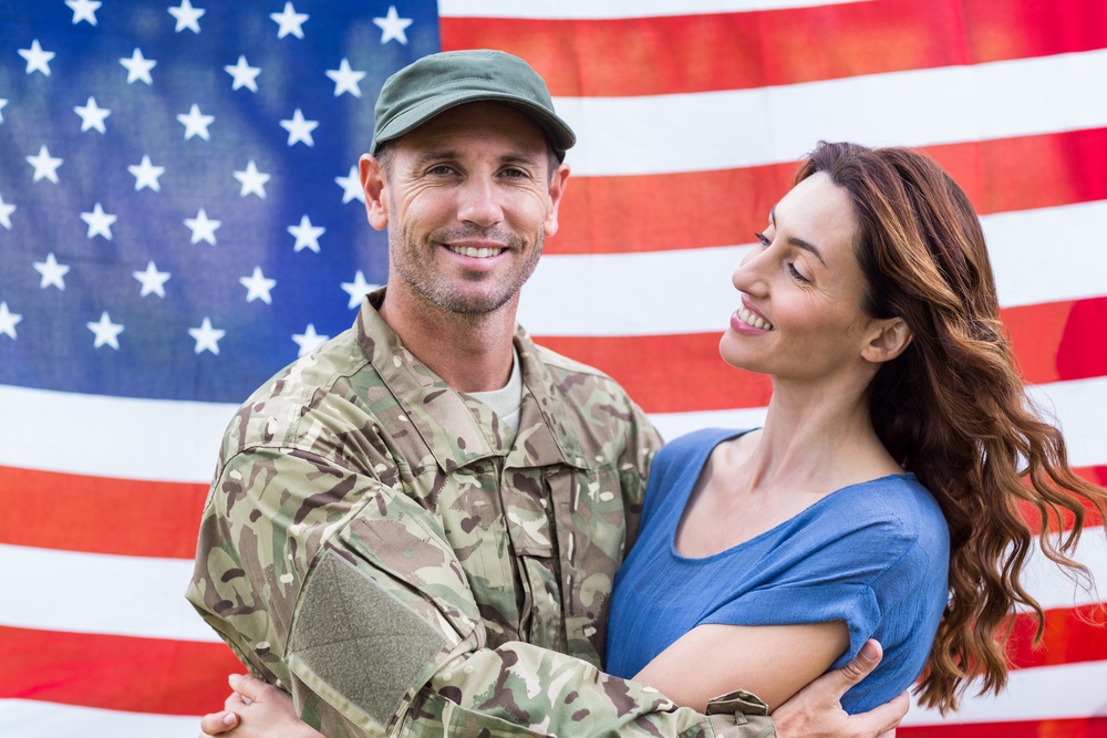 Soldier with partner smiling with American flag in the background