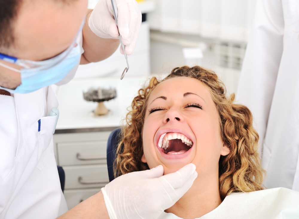 Overcoming fear of the dentist - Happy woman smiling while a dentist checks her teeth