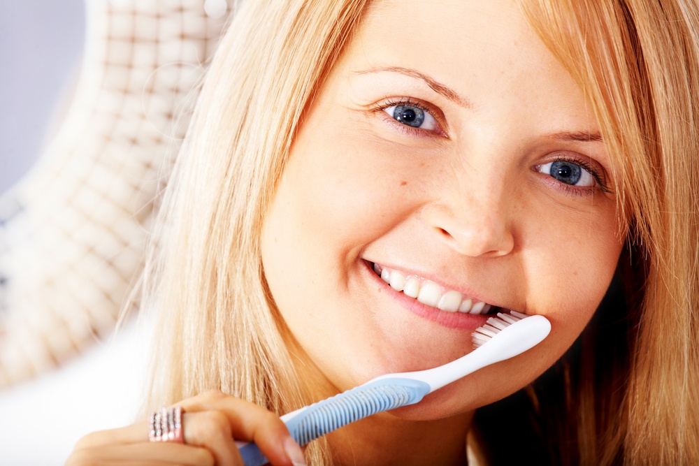 Woman brushing her teeth by a mirror